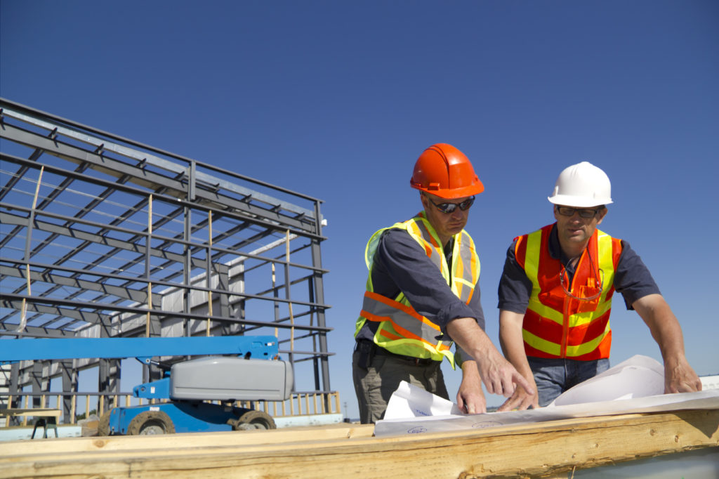 Construction inspectors in hard hats reviewing plans beside a steel frame