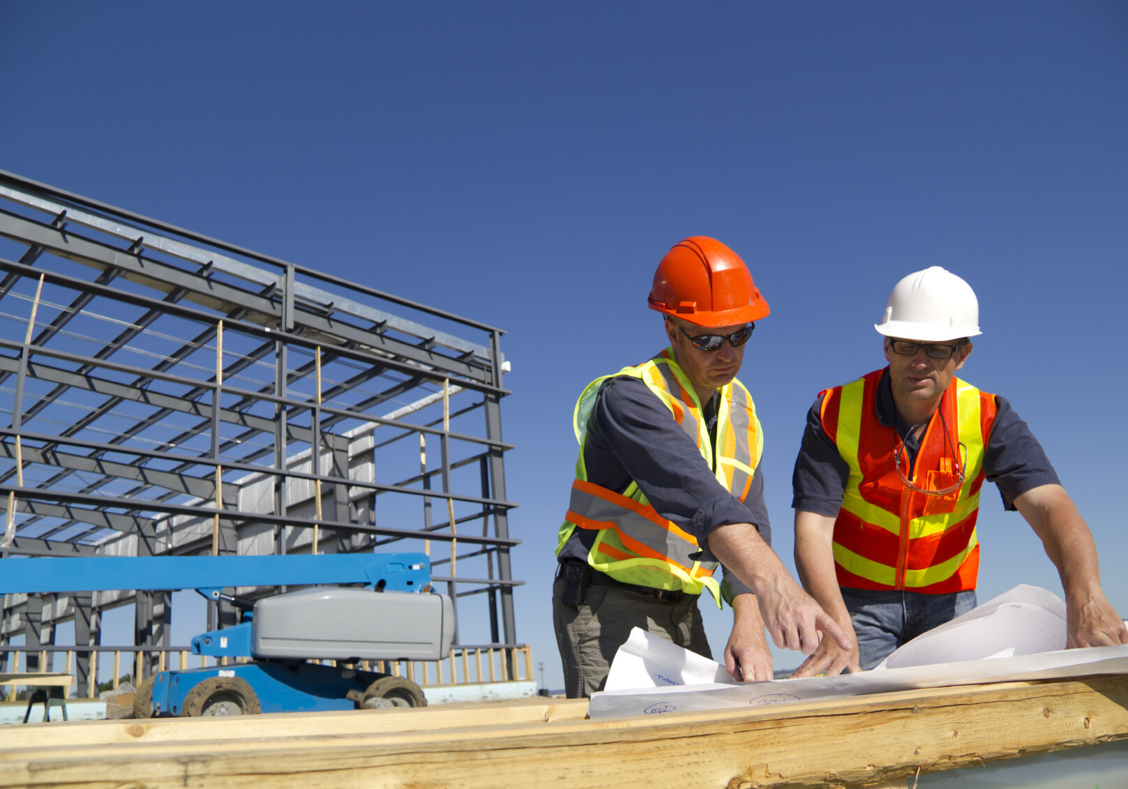 Construction workers looking over plans with a building under construction behind them