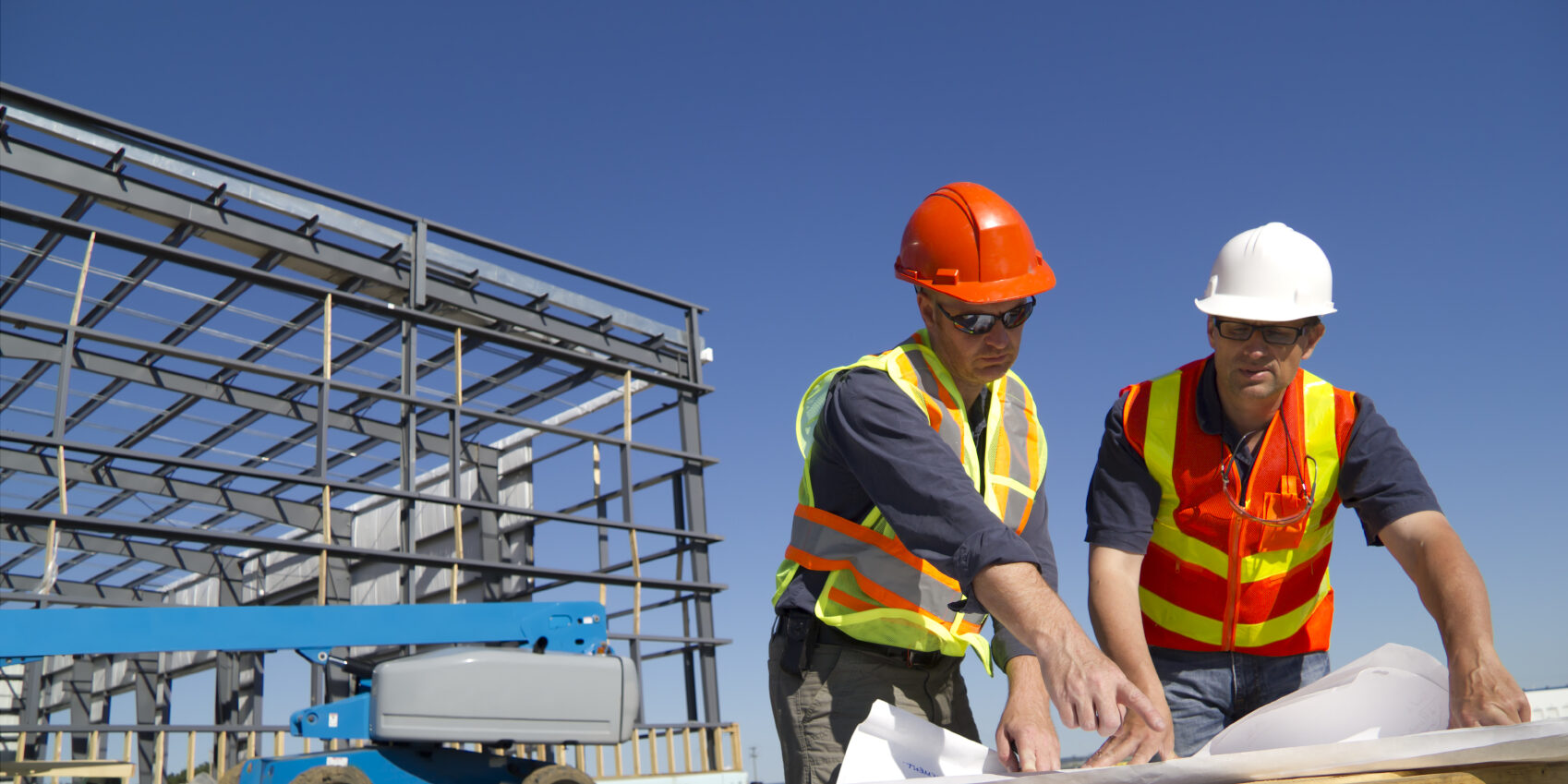 Construction workers looking over plans with a building under construction behind them